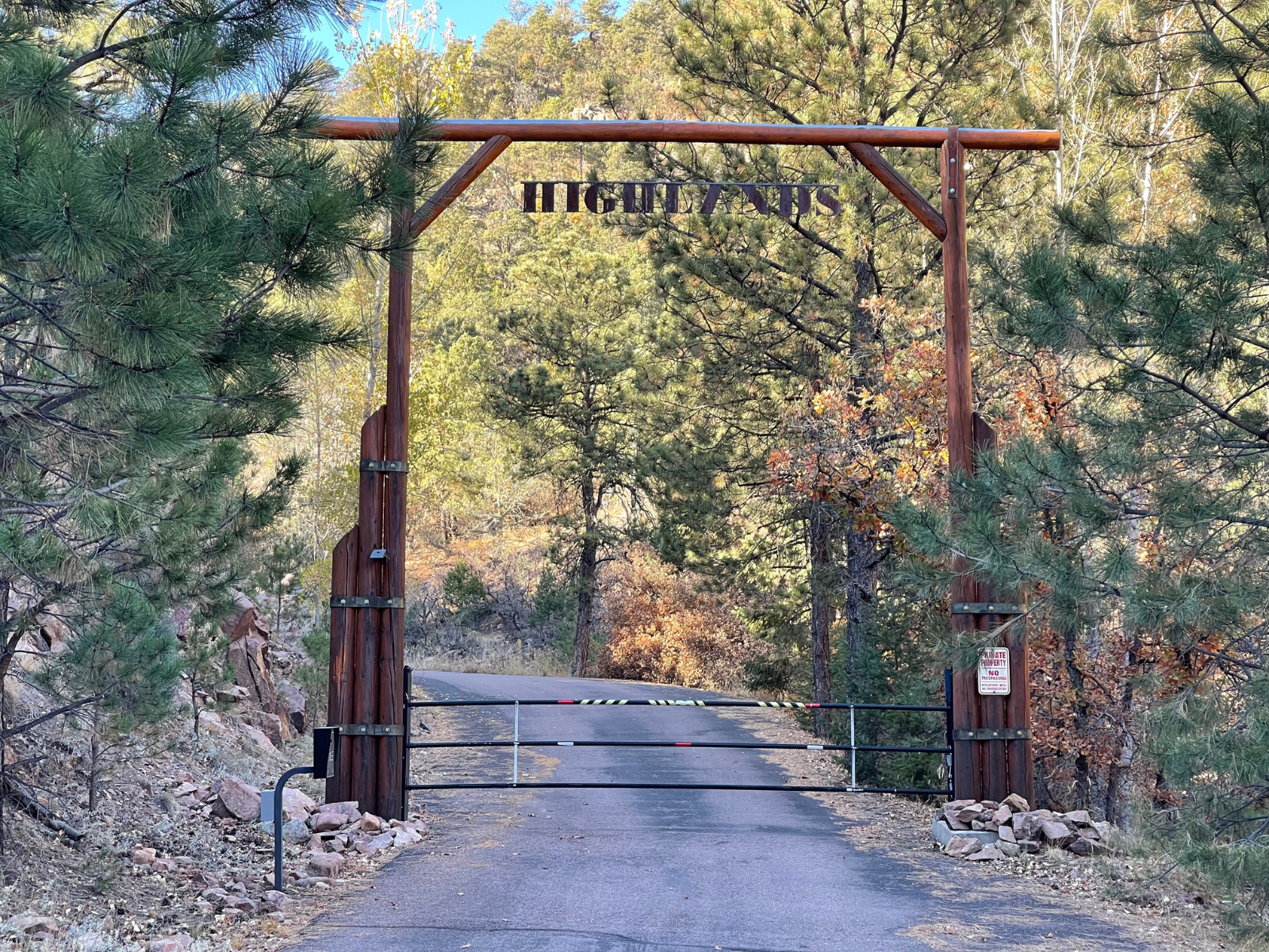 The wooden entry arch and gate where the paved private road runs uphill into the Ranch.
